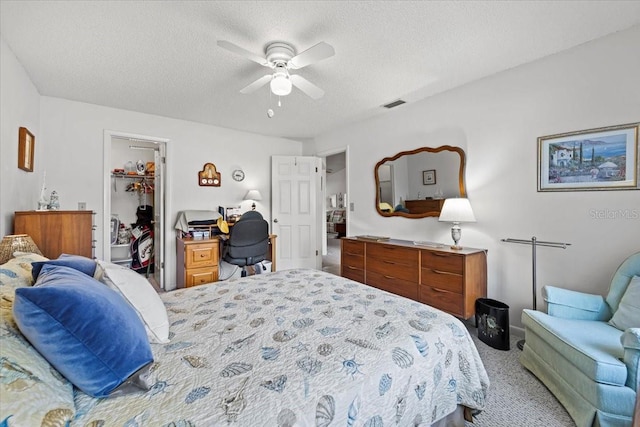 carpeted bedroom featuring a closet, ceiling fan, a walk in closet, visible vents, and a textured ceiling