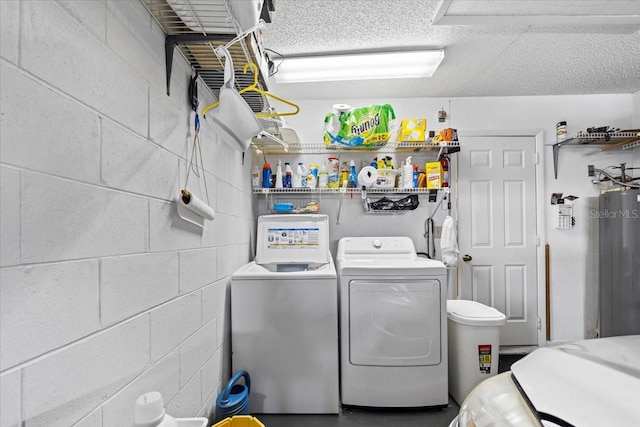laundry room with water heater, laundry area, concrete block wall, washing machine and dryer, and a textured ceiling