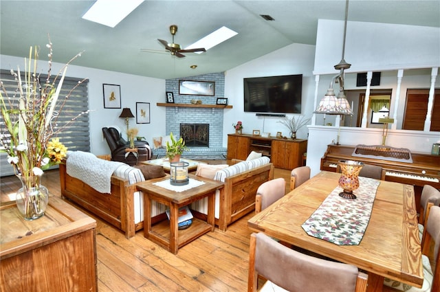 living room with a ceiling fan, lofted ceiling with skylight, a fireplace, visible vents, and light wood-style floors