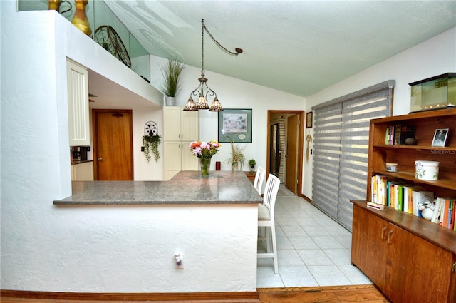 kitchen featuring lofted ceiling, light tile patterned floors, hanging light fixtures, an inviting chandelier, and a peninsula