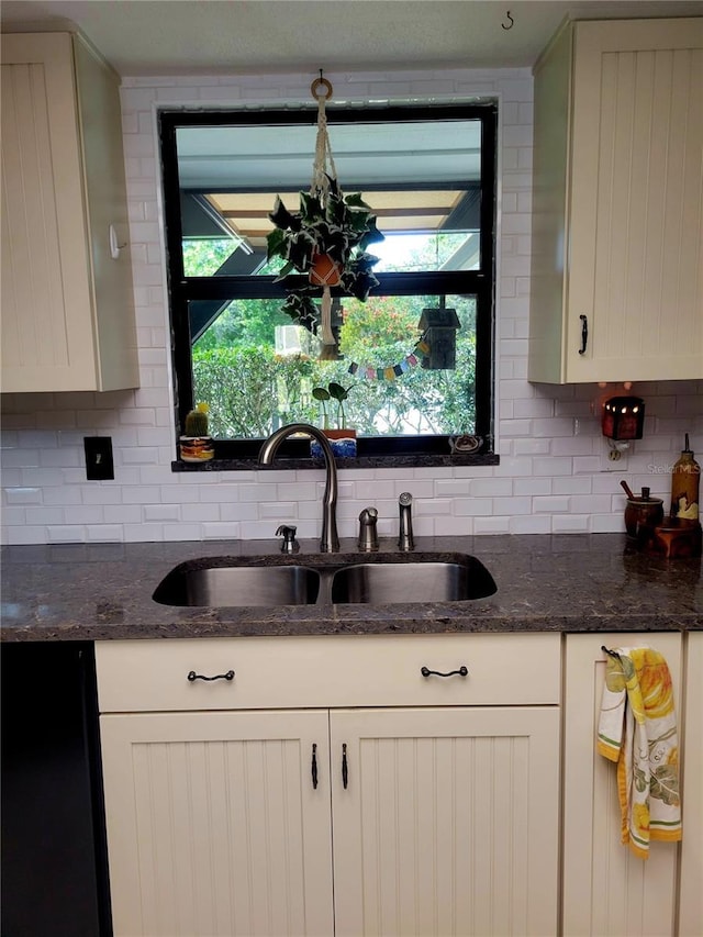 kitchen with backsplash, dark stone counters, white cabinetry, and a sink