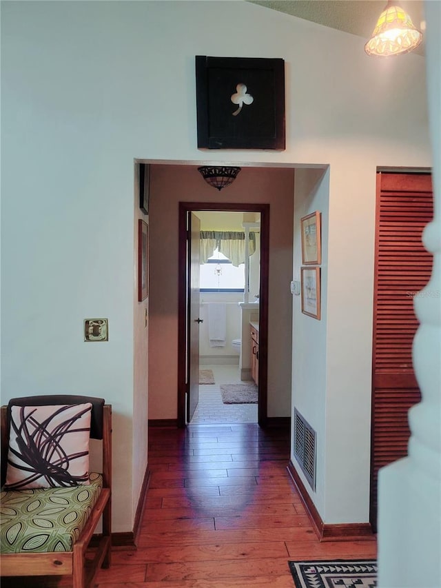 hall with baseboards, visible vents, and wood finished floors