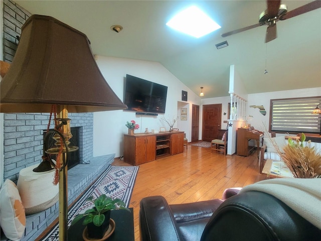 living room with visible vents, ceiling fan, vaulted ceiling, light wood-style floors, and a fireplace