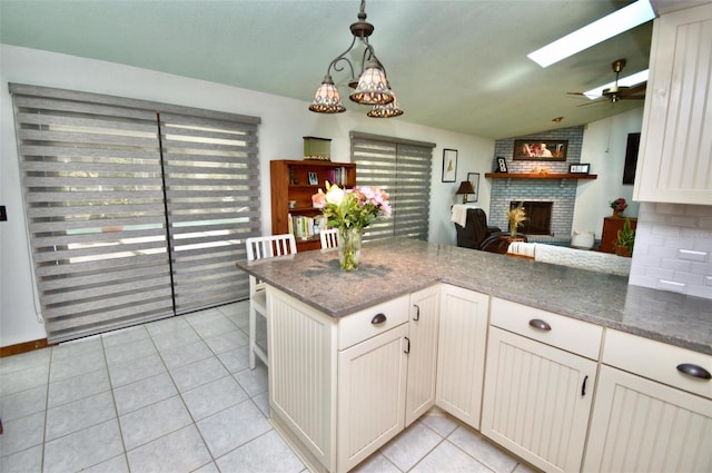 kitchen with a peninsula, lofted ceiling with skylight, a fireplace, open floor plan, and light tile patterned flooring