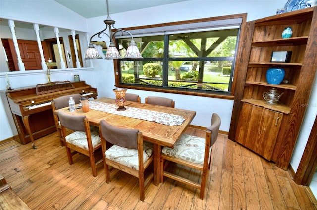 dining area featuring light wood finished floors, lofted ceiling, baseboards, and an inviting chandelier