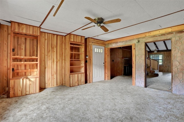 interior space with ceiling fan, wood walls, and carpet flooring