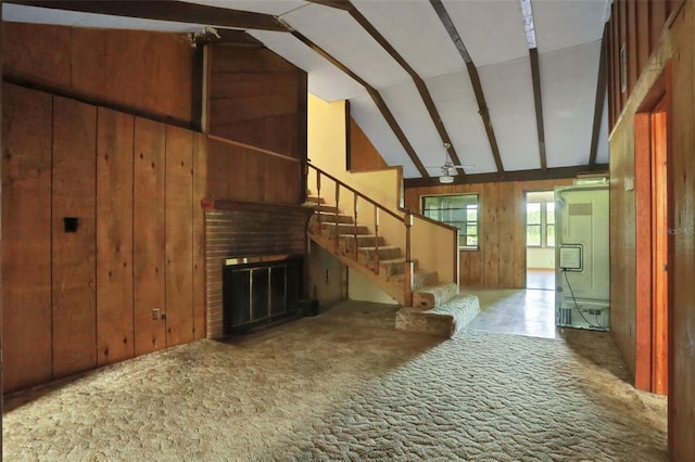 interior space with carpet, lofted ceiling, a brick fireplace, stairs, and wooden walls