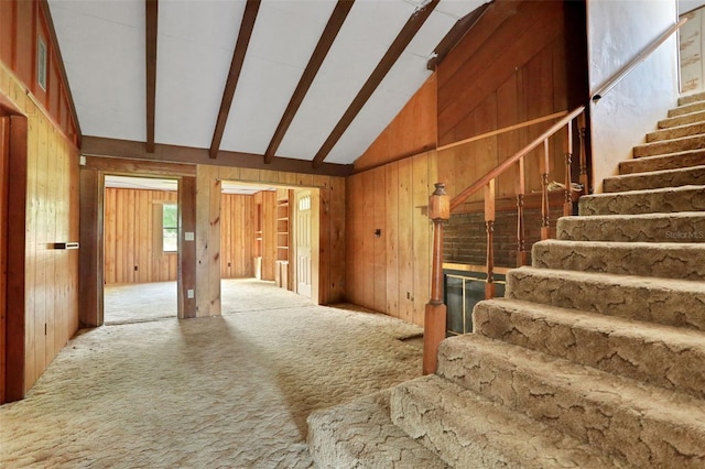 interior space with beam ceiling, wood walls, carpet floors, and high vaulted ceiling