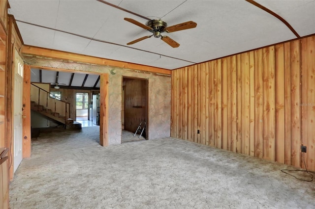carpeted spare room with stairway, a ceiling fan, and wood walls