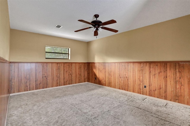 unfurnished room with wood walls, a wainscoted wall, visible vents, and ceiling fan