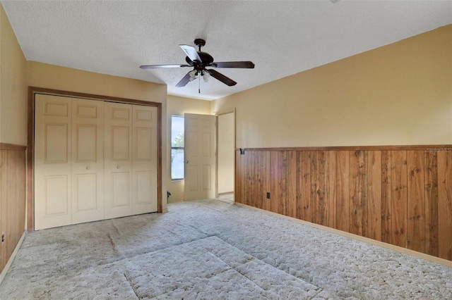 unfurnished bedroom featuring wainscoting, a textured ceiling, wooden walls, and carpet