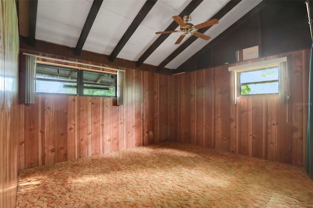 carpeted spare room featuring ceiling fan, wood walls, and lofted ceiling with beams