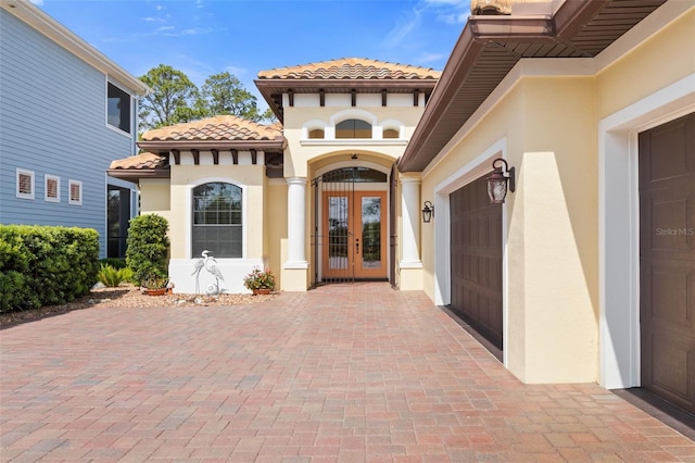 doorway to property with stucco siding, a garage, french doors, and a tile roof