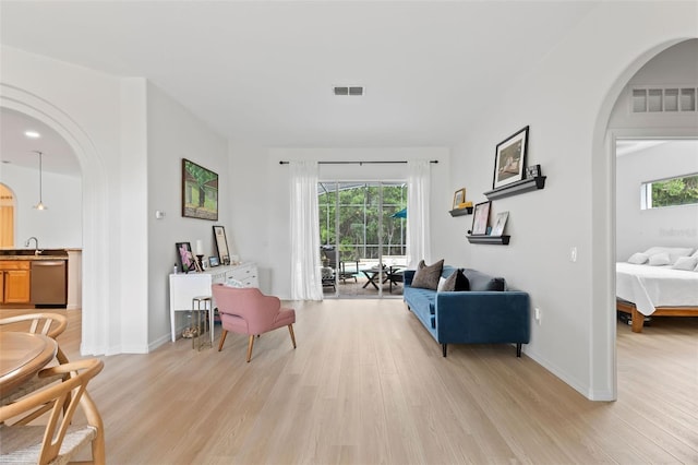 living room featuring light wood-style floors, a healthy amount of sunlight, visible vents, and arched walkways