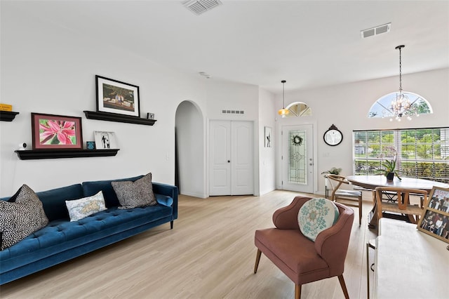 living area featuring a notable chandelier, arched walkways, visible vents, and light wood-style flooring