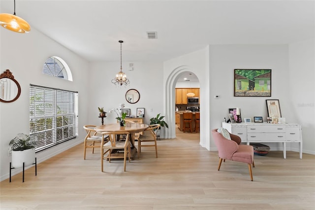dining space with light wood finished floors, a chandelier, visible vents, baseboards, and arched walkways