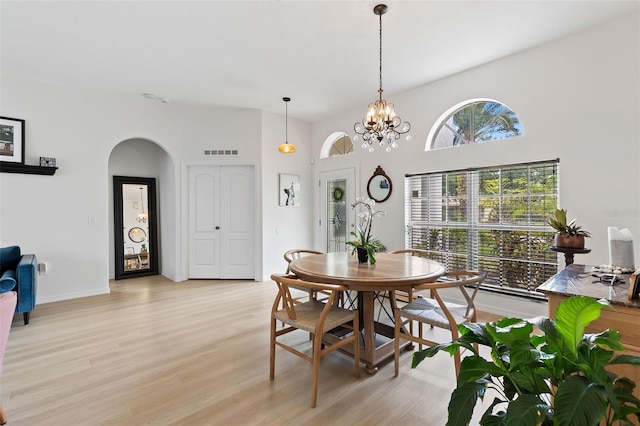 dining area featuring visible vents, arched walkways, light wood-type flooring, and a notable chandelier