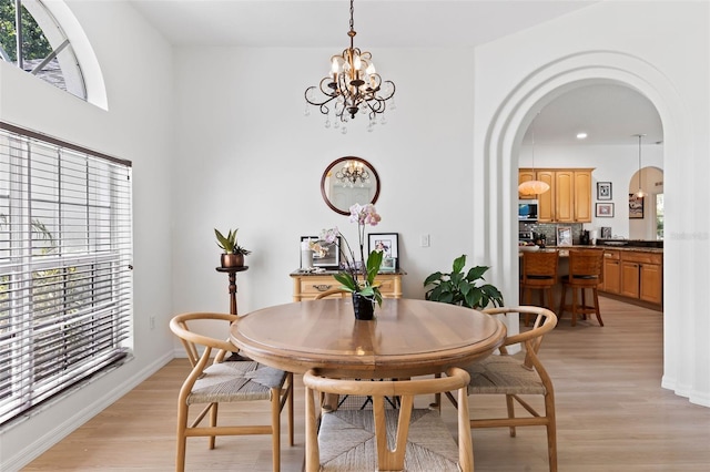 dining area with arched walkways, light wood-style floors, a chandelier, and plenty of natural light