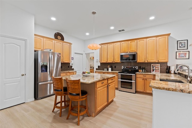 kitchen featuring light stone counters, a sink, appliances with stainless steel finishes, and light wood-type flooring