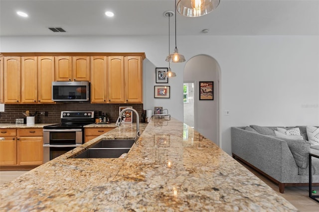 kitchen with a sink, appliances with stainless steel finishes, visible vents, arched walkways, and light stone countertops