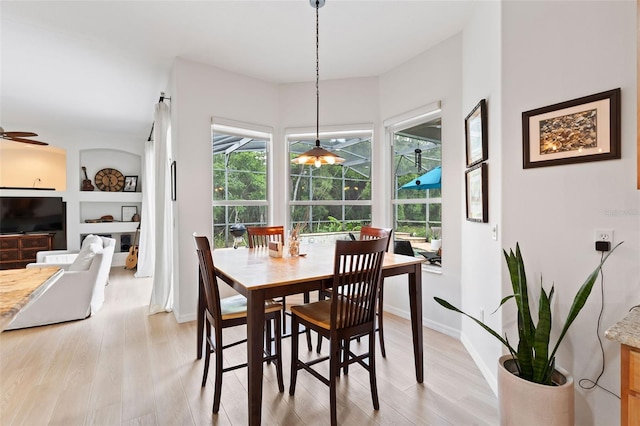 dining room featuring light wood-style floors, baseboards, a sunroom, a ceiling fan, and built in shelves