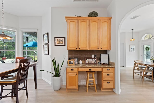 kitchen with arched walkways, light stone counters, built in study area, light wood finished floors, and visible vents
