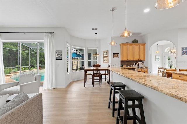 kitchen with a kitchen breakfast bar, visible vents, arched walkways, light brown cabinetry, and light wood finished floors