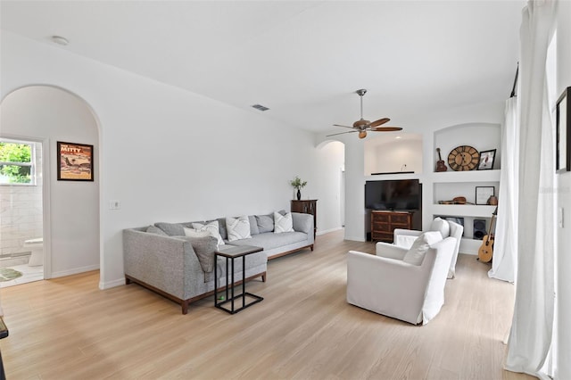 living room with light wood finished floors, arched walkways, visible vents, and ceiling fan