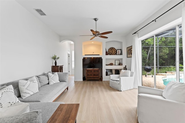 living area with arched walkways, visible vents, ceiling fan, and light wood-style flooring