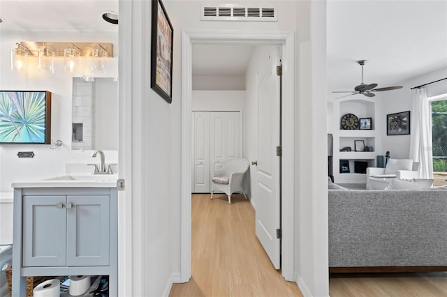 hall featuring visible vents, light wood finished floors, built in features, and a sink