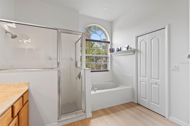 bathroom featuring a stall shower, a bath, wood finished floors, and vanity