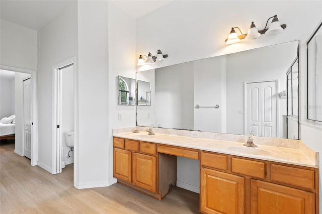 bathroom featuring a sink, toilet, double vanity, baseboards, and wood finished floors