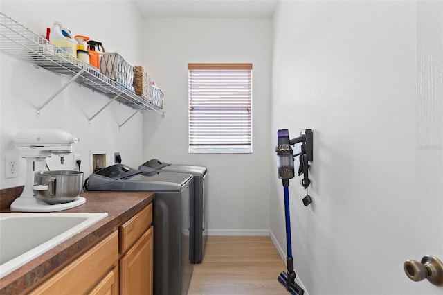 clothes washing area featuring independent washer and dryer, a sink, light wood-style floors, baseboards, and cabinet space