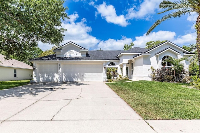 ranch-style home with driveway, a shingled roof, a front yard, an attached garage, and stucco siding