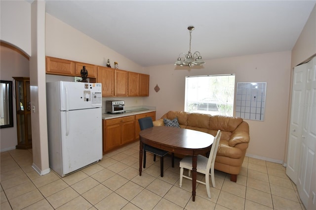 kitchen with an inviting chandelier, light countertops, brown cabinetry, freestanding refrigerator, and light tile patterned floors