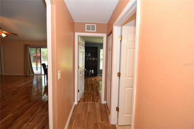corridor featuring visible vents, baseboards, and wood finished floors