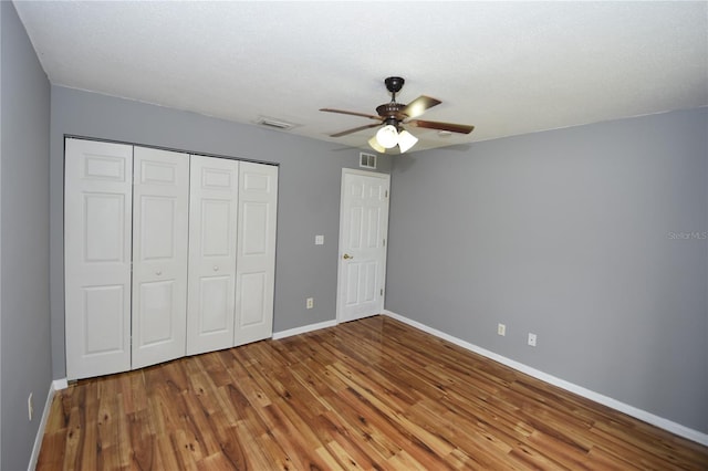 unfurnished bedroom featuring ceiling fan, visible vents, wood finished floors, baseboards, and a closet