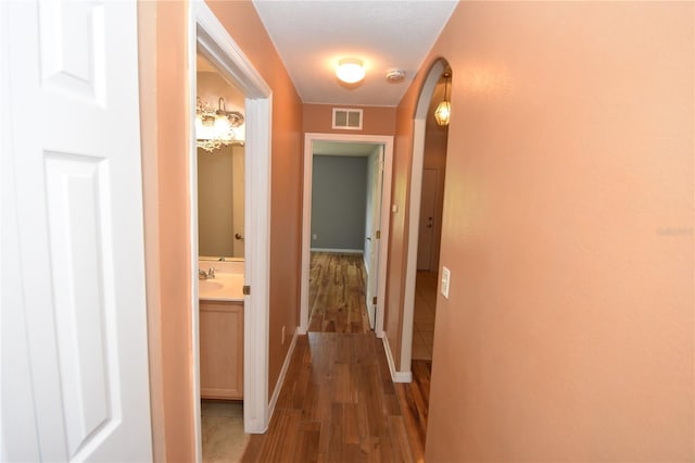 corridor with arched walkways, baseboards, visible vents, and wood finished floors