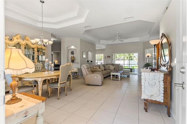 living area featuring ceiling fan with notable chandelier, a tray ceiling, light tile patterned flooring, and visible vents