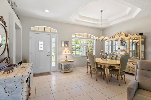 foyer entrance featuring visible vents, light tile patterned floors, a raised ceiling, baseboards, and an inviting chandelier