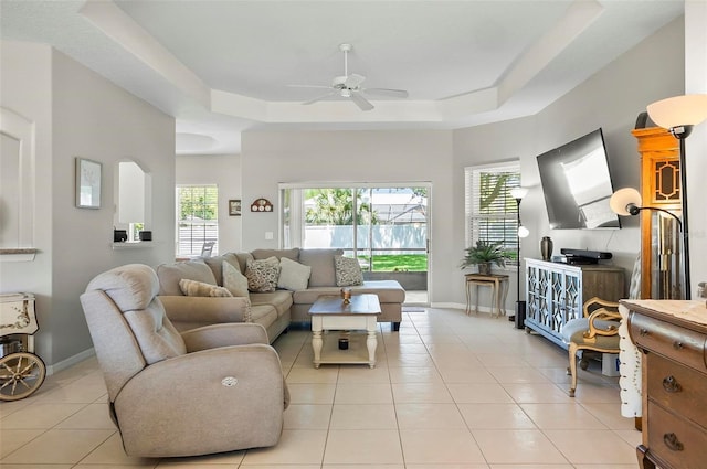 living room with a ceiling fan, a tray ceiling, plenty of natural light, and light tile patterned floors