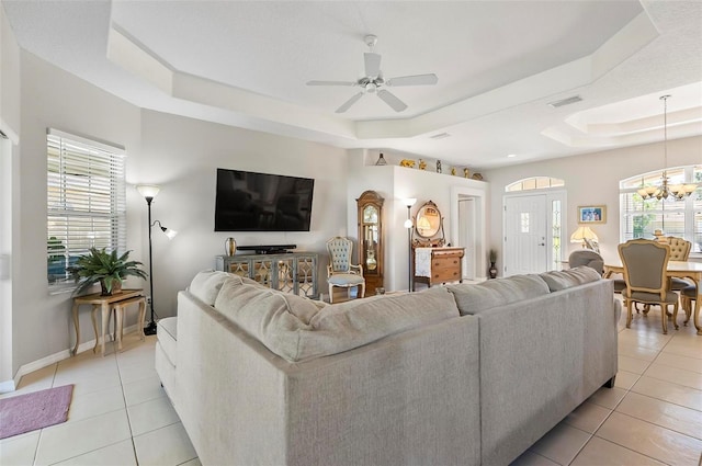 living area featuring visible vents, ceiling fan with notable chandelier, light tile patterned floors, and a tray ceiling