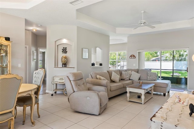 living room with light tile patterned flooring, a ceiling fan, visible vents, and a tray ceiling