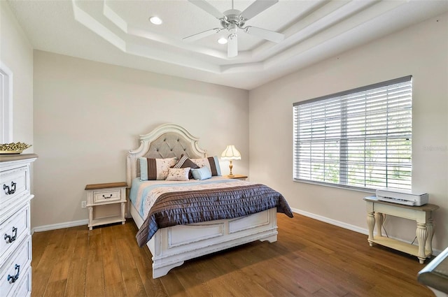 bedroom with wood finished floors, baseboards, recessed lighting, a raised ceiling, and a ceiling fan