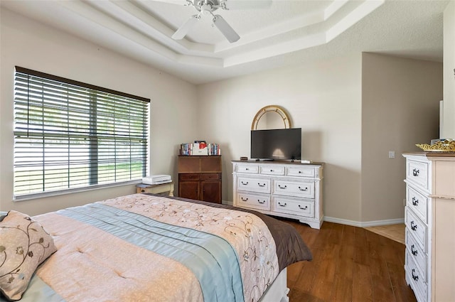 bedroom featuring baseboards, a ceiling fan, wood finished floors, and a tray ceiling