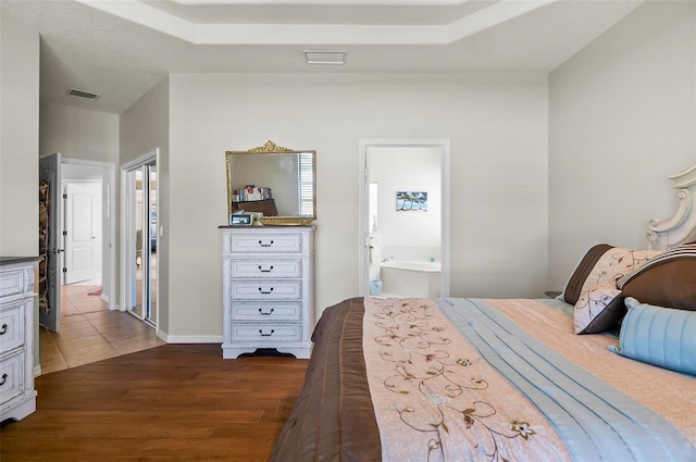 bedroom featuring baseboards, dark wood-style flooring, ensuite bath, and visible vents