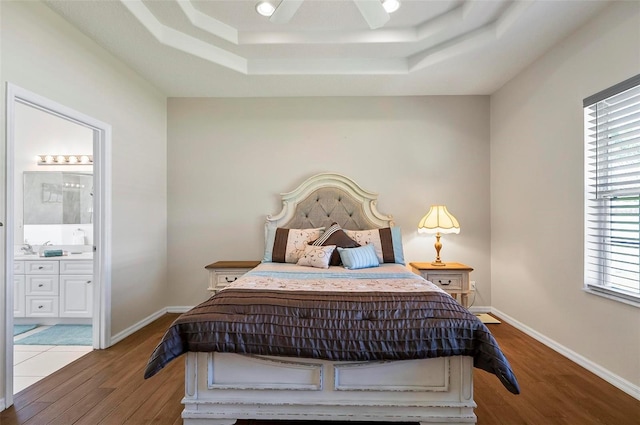 bedroom featuring baseboards, a tray ceiling, wood finished floors, and ensuite bathroom