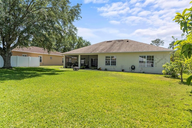 rear view of house featuring a lawn, fence, stucco siding, and a shingled roof