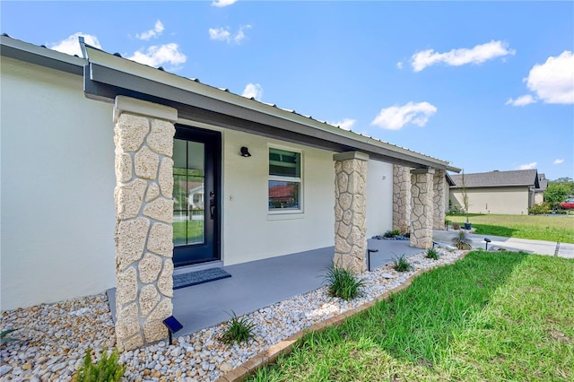 77 Freeport Ln, Palm Coast, FL 32137 - property entrance with stucco siding, stone siding, a porch, and a yard