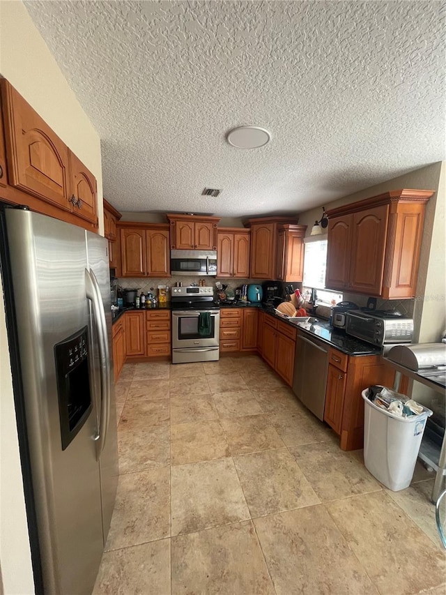 1501 Lambert Ave, Flagler Beach, FL 32136 - kitchen featuring appliances with stainless steel finishes, brown cabinets, dark countertops, and a textured ceiling